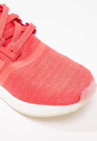 Červená sportovní obuv s texturovaným pleteným svrškem, plochými tkaničkami, zesílenou špičkou a bílou polstrovanou podešví.