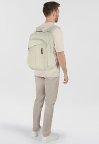 Zaino grigio chiaro con chiusura a doppia cerniera, spallacci regolabili e logo anteriore. Texture liscia, forma rettangolare e tasca laterale in rete.