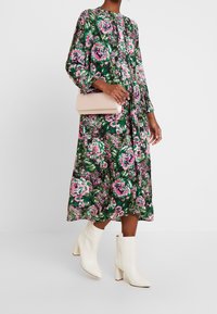 Vestido floral en verde, rosa y blanco, con mangas largas y una falda plisada. Combinado con un bolso de mano rosa claro y botas de tacón bloque blancas.