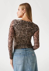 Tee a maniche lunghe in mesh con un design a stampa di serpente marrone, abbinata a una gonna in denim azzurro chiaro con tasche posteriori e dettaglio del logo.