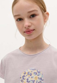 Lichtpaarse T-shirt met korte mouwen, met een cirkelvormig, multikleurig luipaardprintontwerp. Zachte stof met een ronde hals.