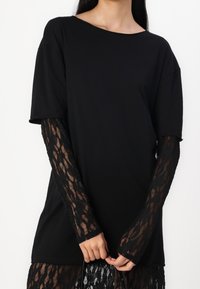 Zwarte korte mouwen top met een wijd decolleté, gecombineerd met aansluitende zwarte kanten lange mouwen met een bloemenpatroon en sheer textuur.