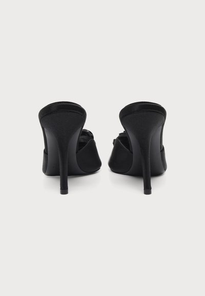 Paire de chaussures mules noires à talons hauts vues de dos sur un fond clair uni.