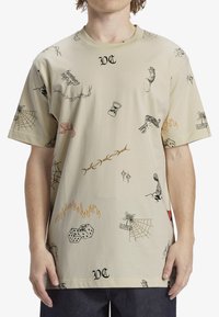 Camiseta beige con varias estampaciones gráficas, incluyendo dados, llamas y telarañas. Mangas cortas y un escote redondo.