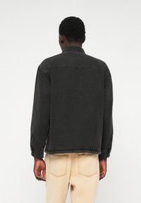 Veste en denim noir avec un col, un ourlet élastique et des poches latérales. Présente une texture lisse et un design de coutures simples.