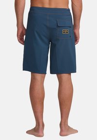 Pantaloni da bagno blu da uomo realizzati in materiale leggero, con una tasca posteriore con etichetta, cuciture in contrasto e un taglio dritto.