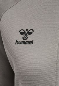 Gros plan sur un tissu gris texturé avec le logo hummel noir comportant un emblème d'abeille stylisé et le nom de la marque sur le vêtement.