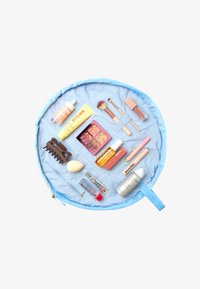 Bolsa de maquillaje redonda de tela azul claro, que contiene varios productos de belleza, incluyendo una paleta de maquillaje, brochas y productos para el cuidado de la piel.