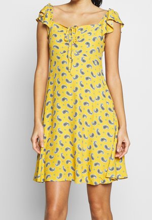Robe jaune avec un motif cachemire, manches froncées, décolleté carré et un détail noué à l'avant. Silhouette en A, longueur genoux.