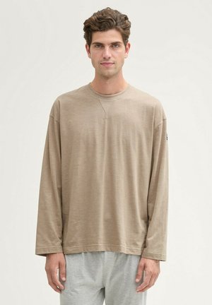 Beige Langarm-T-Shirt aus weichem Stoff, mit Rundhalsausschnitt und entspannter Passform, kombiniert mit hellgrauen Jogginghosen.