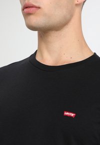 Zwarte t-shirt met korte mouwen, gemaakt van zachte katoen. Heeft een klein rood Levi's-logo op de linkerkant van de borst. Rondhals ontwerp.
