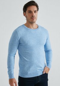 Pull en tricot bleu clair avec un décolleté rond et des manches longues. Tissu texturé avec des poignets et un ourlet côtelés. Assorti avec un jean foncé.