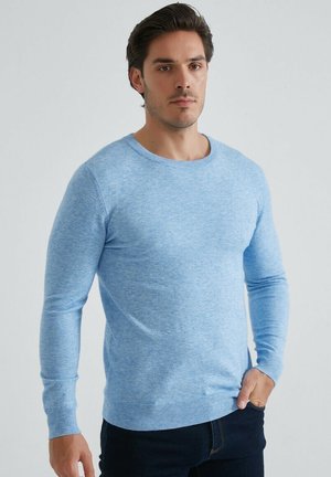 Pull en tricot bleu clair avec un décolleté rond et des manches longues. Tissu texturé avec des poignets et un ourlet côtelés. Assorti avec un jean foncé.