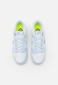 Ljusblå och vita sportskor med perforerad tåbox, platta snören och klara gröna innersulor med blommönster.