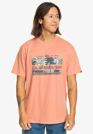 Short-sleeve coral t-shirt made of cotton. Features a graphic print with tropical leaves and the "Quiksilver" logo at the center.