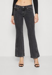 Jeans de mezclilla negra acampanados con una cintura alta, que cuentan con un cierre de cremallera, botón y herrajes en tono cobre, presentando un diseño clásico.