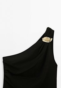 Black one-shoulder top with a gold leaf-shaped metal clasp on the strap against a plain white background.
