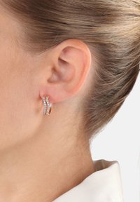 Pendientes de aro en oro rosa con un diseño ondulado, que presentan un acento de pequeñas piedras transparentes a lo largo de un lado. Acabado suave, grosor medio.