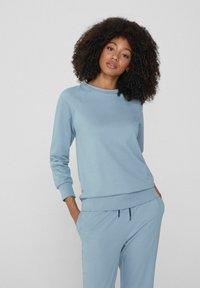 Světle modrý svetr vyrobený z měkkého materiálu, s kulatým výstřihem, dlouhými rukávy a volným střihem. Hladký povrch s žebrovanými zápěstími.