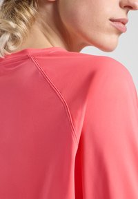 Top a maniche corte di un vivace rosa corallo, caratterizzato da una texture liscia, dettagli di cucitura sottile e una vestibilità rilassata nella cucitura della spalla.