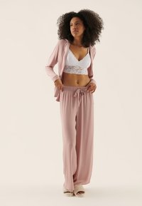 Light pink lounge set with long, loose pants and a short, open-front hoodie. White lace bralette underneath. Soft, smooth texture.