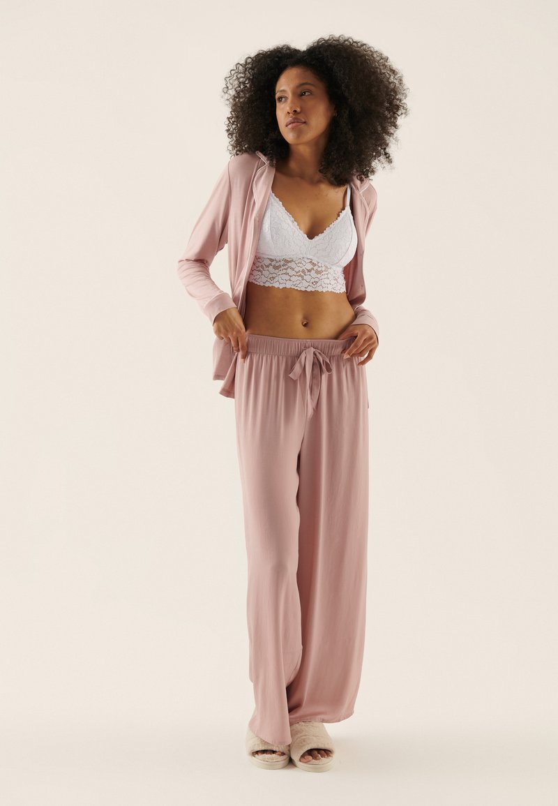 Light pink lounge set with long, loose pants and a short, open-front hoodie. White lace bralette underneath. Soft, smooth texture.