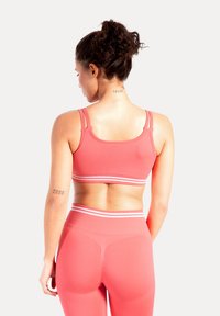 Koralowy sportowy biustonosz z szerokimi ramiączkami i białymi akcentami, zestawiony z pasującymi legginsami z wysokim stanem o teksturowanym wykończeniu i bezszwowej konstrukcji.