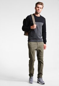 Sivý a čierny svetrový top s dlhými rukávmi, khaki nohavice a sivé tenisky. Modelka má na sebe pieskovú batoh.