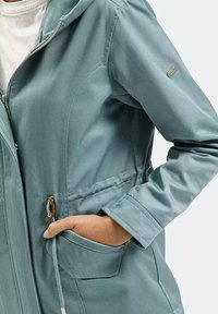 Jasnozielona kurtka z kapturem, z zapięciem na zamek błyskawiczny, przednimi kieszeniami oraz sznurkiem w talii. Gładki materiał, minimalistyczny design.