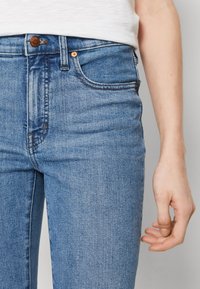 Jeans de mezclilla azul con corte recto, con cierre de botón y cremallera, diseño de cinco bolsillos y un ligero desgastado a lo largo de los muslos.