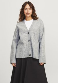 Cardigan gris avec un col en V, des manches longues et un ourlet côtelé. Présente cinq boutons foncés sur le devant et est fabriqué à partir d'un matériau doux et texturé.