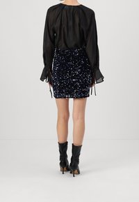 Svart genomskinlig blus med långa ärmar och knytningar, tillsammans med en åtsittande paljettminikjol med blå och silver detaljer. Svarta ankeldubbar.