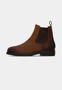 Botas Chelsea de cuero marrón con paneles laterales elásticos, punta redonda y acentos texturizados. Suela de goma negra y una lengüeta para facilitar el calzado.