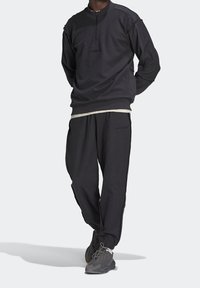 Svart träningströja med halvmudd och broderad logotyp, ihop med matchande joggingbyxor med sidostripes.