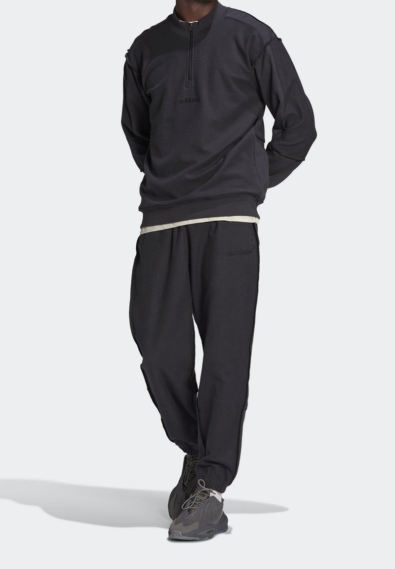 Svart träningströja med halvmudd och broderad logotyp, ihop med matchande joggingbyxor med sidostripes.