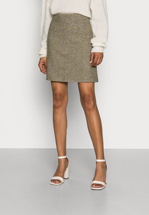 Ruskeakermanvärinen houndstooth-kuvioitu suora hame, yhdistettynä valkoisiin lohkopohjaisiin sandaaleihin. Pehmeä, teksturoitu kangas.