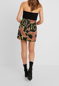 Haut noir sans bretelles associé à une mini-jupe avec un motif chaîne vibrant rose et jaune sur fond noir.