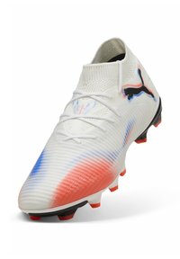 Botín de fútbol blanco con acentos en degradado azul y rojo, parte superior texturizada, diseño de tobillo alto y suela negra con tacos naranjas.