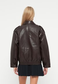 Veste en cuir marron avec une coupe décontractée, dotée d'épaules épaulettes et d'un ourlet élastiqué, présentée de dos sur fond blanc.