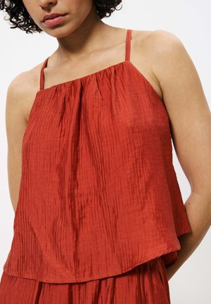 Haut sans manches rouge à coupe décontractée, avec des plis verticaux et des bretelles fines. Le tissu a une finition douce et texturée.