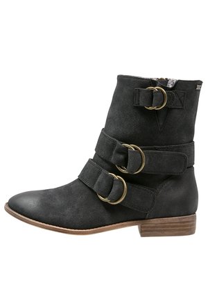 Stivaletto in suede nero con due ampie cinghie, ognuna con una fibbia rotonda in tono oro. Tacco basso impilato e design a punta.