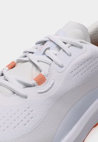 Κοντινή λήψη λευκού αθλητικού παπουτσιού με υφασμάτινη υφή, λευκά κορδόνια, πορτοκαλί θηλιές κορδονιών και ανάγλυφο λογότυπο Nike στο πλάι.