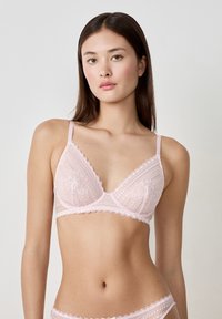 Bralette triangolare in pizzo rosa pastello, con bordi scallop, sottili spalline regolabili e motivi floreali sul tessuto.