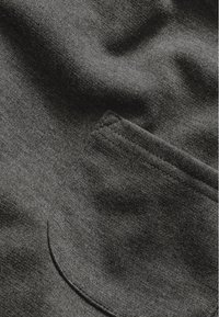 Dunkelgrauer Stoff mit weicher Textur, auf dem eine kleine aufgenähte Brusttasche angebracht ist, die das glatte, gleichmäßige Gewebe hervorhebt.