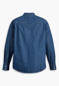 Camisa de mezclilla en azul oscuro, con mangas largas, cuello puntiagudo y dobladillo curvado. La parte trasera tiene un detalle de yugo con una ligera forma de V.