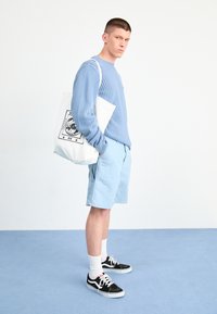 Maglione lavorato a maglia azzurro chiaro, pantaloni shorts azzurro chiaro coordinati, sneakers nere con suola bianca e una borsa a tracolla bianca con stampa grafica.