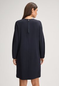Marineblauwe shift dress met lange mouwen, ritsdetail aan de achterkant en franjesaccent. Gemaakt van een soepele, lichtjes gestructureerde stof, knielang.