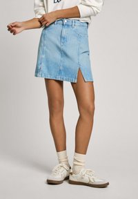 Light blue denim mini skirt featuring a front slit, classic five-pocket design, and a waistband with belt loops.