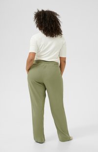 Loose-fitting olive green pants in lightweight fabric with an elastic waistband. Smooth texture and wide leg design, worn with a light top.