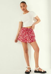Rød blomsterprint nederdel med elastisk liv, parret med en hvid tætsiddende t-shirt med korte ærmer og beige platform sandaler. Glat tekstur.